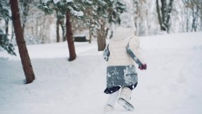 Cheerful children are running through the snow and playing together in the park in the winter around trees. Slow motion