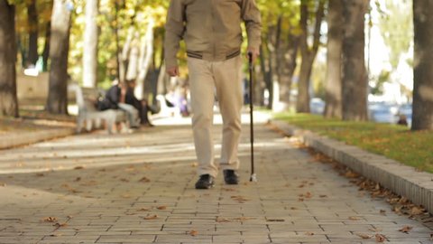 Fall, weak grandad limping slowly, carefully along parkway, leaning on old cane