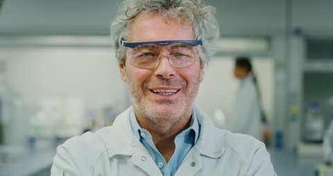Portrait of smiling male scientist wearing protection glasses satisfied with great results of completed research in laboratory. Shot in 8K. Concept: research,biochemistry, pharmaceutical medicine