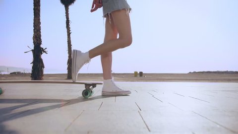 Young beautiful female skater girl long fit legs in mini jeans skirt are ready to go staying or riding skateboard or longboard in summer hot day. Waiting to strat enjoy skateboarding and active sport