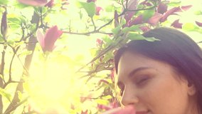 Beauty young woman enjoying nature and touching spring magnolia flowers, Happy Beautiful girl in Garden with blooming magnolia trees. Model smelling blossom, slow motion 4K UHD video