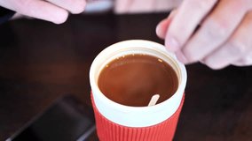Clip taken at coffee shop cafe of a caucasian women stirring and drinking from a refillable cup with hot coffee or tea in it. Shot in 4k 60fps and slowed down to 50% on a 30fps timeline.