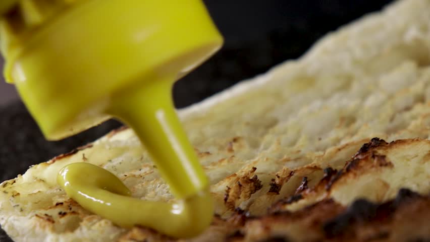 Extreme close up of mini ciabatta loaf being topped with mustard.