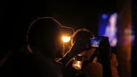 Unrecognizable man silhouette taking photo or recording video of live music concert with smartphone at night. Photography, entertainment and technology concept