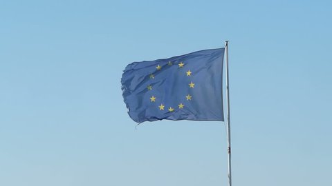 Frayed European Union (EU) flag is fluttered by a strong wind, blue sky background
