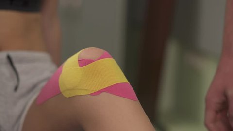 A close-up of hands rubbing kinesiotape placed on the knee. A therapist is kinesiotaping a knee joint if the anterior cruciate ligament is injured.