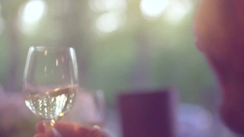 Group of people toasting and drinking white Wine on the restaurant terrace over sunset. Friends Celebrating. Glasses with wine over nature Background. Holiday. Resort. 4K UHD video 3840X2160 