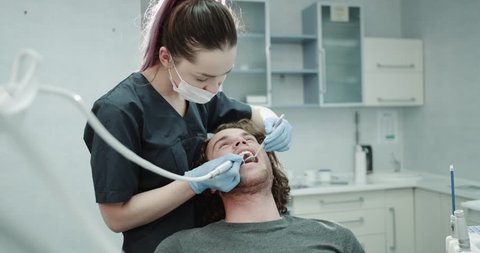 Closeups in a modern clinic room dentis make a oral hygiene procedure to the young man patient , in the dental room. 4k Video Stok