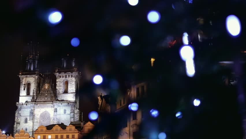 Prague, Czech Republic - December 2018: Gothic Church revealed from behind the Christmas tree glowing at night. Old Town Square. 4K resolution trucking shot.