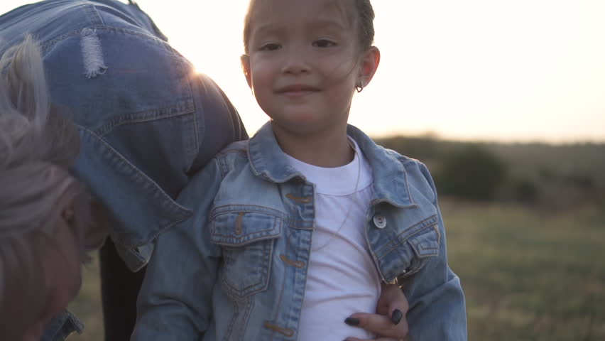 Cute little asian girl looking at camera. Close up shot. Mixed race family, european mother and asian daughter spending time in the park on sunset. Warm spring or summer season