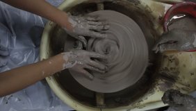 A close up video clip of two sets of hands playing with a mess of clay on a pottery wheel.