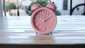 Pink alarm clock on wooden board. Tracking shot.