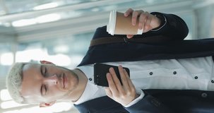 Vertical video. Young attractive businessman standing on the street drinking coffee and using phone near business center