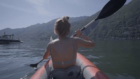 Rear view of a young woman paddling on red canoe in Summer enjoying beautiful mountain lake nature. People travel vacations concept - 4K