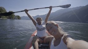 Cheerful couple taking selfie portrait in canoe on mountain lake enjoying Summer holidays - Two young adults having fun in Europe- Slow motion