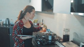 woman cooks soup pan in the kitchen prevents the water in the pot and looks at the recipe on the digital tablet. woman in the kitchen slow motion video. girl mom in lifestyle the kitchen indoors