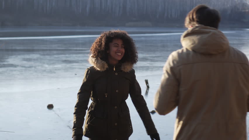 Man photographing woman by frozen lake