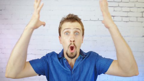 Person is mind blowing by your statement in slow motion HD. Static portrait shot of male person in focus looking into camera and goes mind blown with both hands sinking down out of the frame.