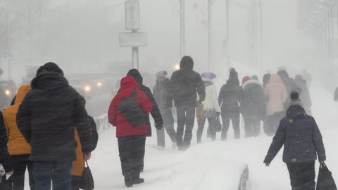 PETROPAVLOVSK CITY, KAMCHATKA PENINSULA, RUSSIA - DEC 28, 2018: People walk through snow on city sidewalk during heavy snowfall, blowing snow, gale during Pacific cyclone, hiding faces from snow storm