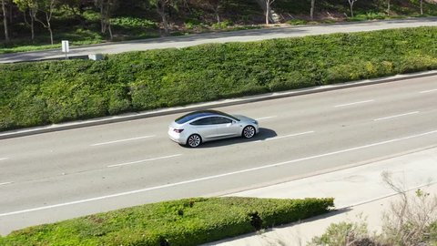 Newport Beach, CA / USA - December 27th 2018: Aerial view of Tesla Model 3 Performance electric vehicle or EV car driving up a street or road on sunny day.