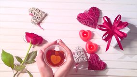Young Couple Hands holding heart shaped tea cup over wooden background. St. Valentine's Day, Love concept. Top view, tabletop. Man giving gift, romance, dating concept. Slow motion 4K