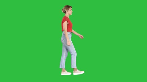 Woman in red t-shirt, jeans and sneakers walking on a Green Screen, Chroma Key.