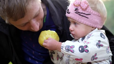 CHERKASY, UKRAINE, OCTOBER 17, 2018: portrait, dad and little daughter. Girl eats a big yellow, sweet pear with big appetite, treats dad. picnic in autumn park. warm autumn day.