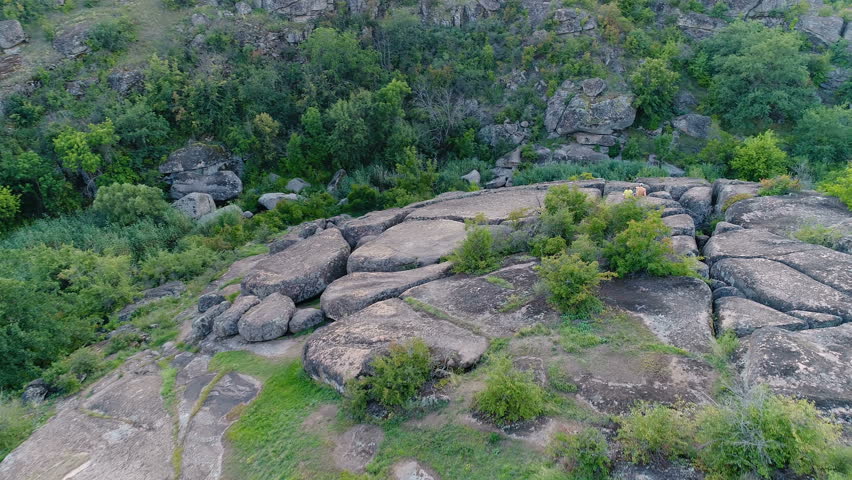 Aerial view in motion of couple sitting on rocky formation with tent and observing landscape enjoying wild trip