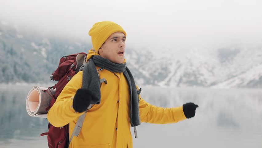 Young hiker man standing on top of the mountain. Traveller man raising hands. Successful and winner Concept. Winter time