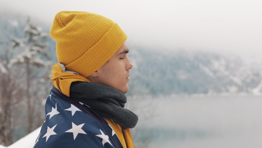 Traveller man with flag of America standing in the snow-covered mountains near beautiful lake. Hiker looking at the beautiful nature