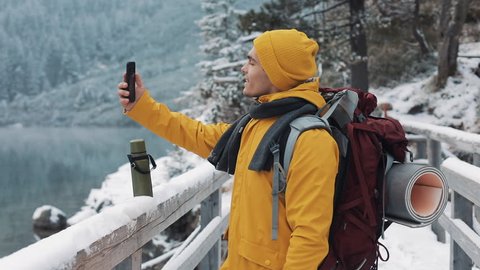 Young traveler man having video chat on winter holiday. Hiker waving at webcam on mobile phone camera sharing his friends winter travel vacation adventure วิดีโอสต็อก