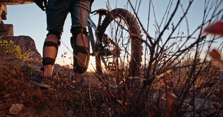 Cool mountain cyclist standing on edge of a mountain or a hill during sunset, ready to ride down and perform stunts - recreational pursuit, getting away from it all 