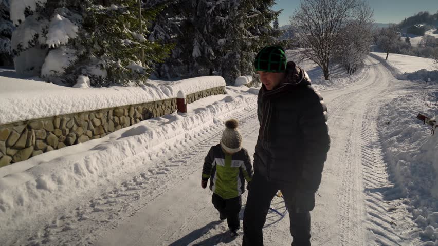 Young happy family having fun playing in a snowy forest. Father rolls his little son on a sled. Dad and his little son are happy together. Winter sunny day.