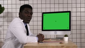 Black doctor talking to camera sitting next to computer screen. White Display.