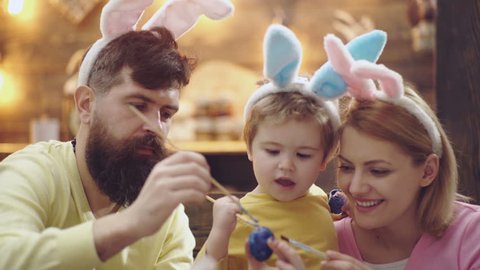 Happy family are preparing for Easter. Cute little boy wearing bunny ears. Concept of Happy Easter. Bearded man with a blond woman and a little boy dressed in a hares ears are painting Easter eggs