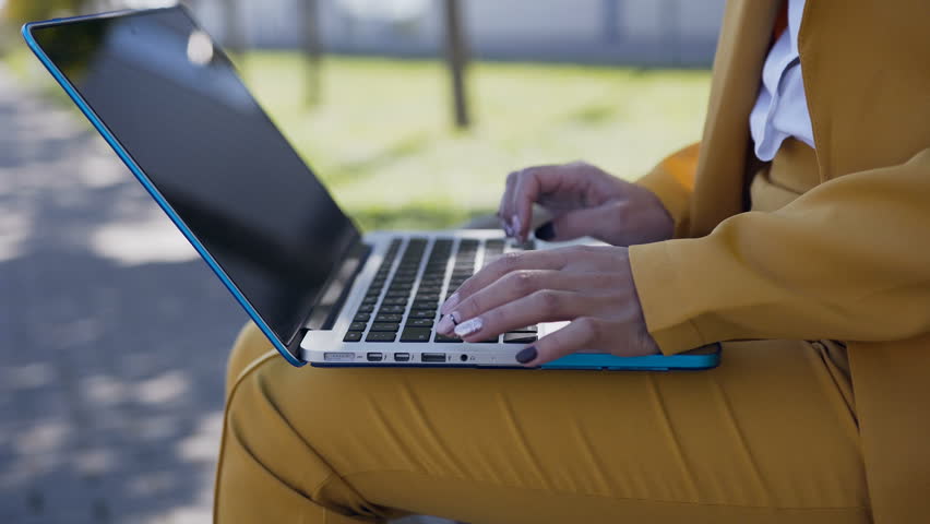 Close-up of a female hands typing on computer keyboard. Outdoors. Young business woman in suit sitting on the bench and hands typing on a computer keyboard,write article,writing report. 4k