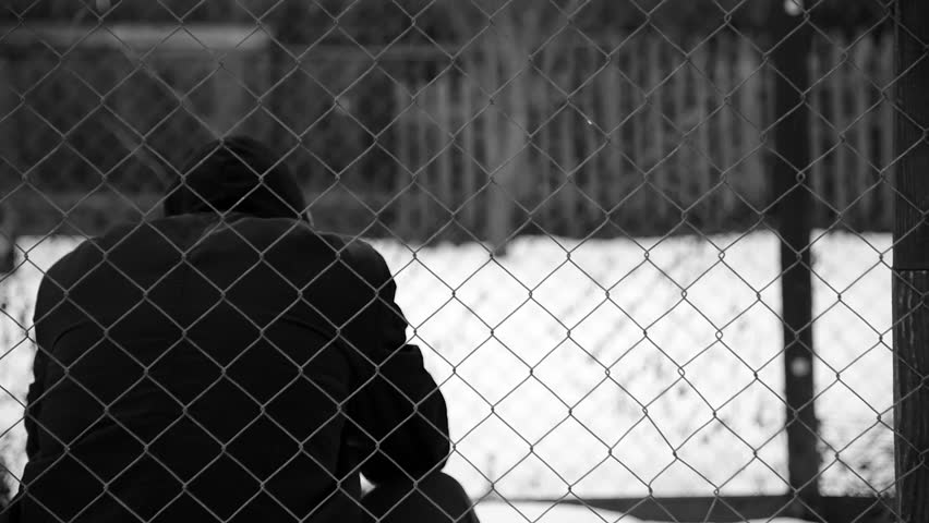 Young unidentifiable teenage boy holding hes head at the correctional institute in black and white, conceptual footage of juvenile delinquency, focus on the wired fence in black and white. Royalty-Free Stock Footage #1021598980