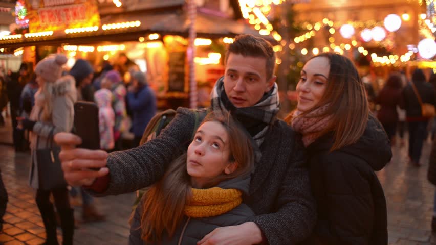 Happy Family with Daughter make via Mobile Phone Selfie Photo on a Christmas Lights City Street