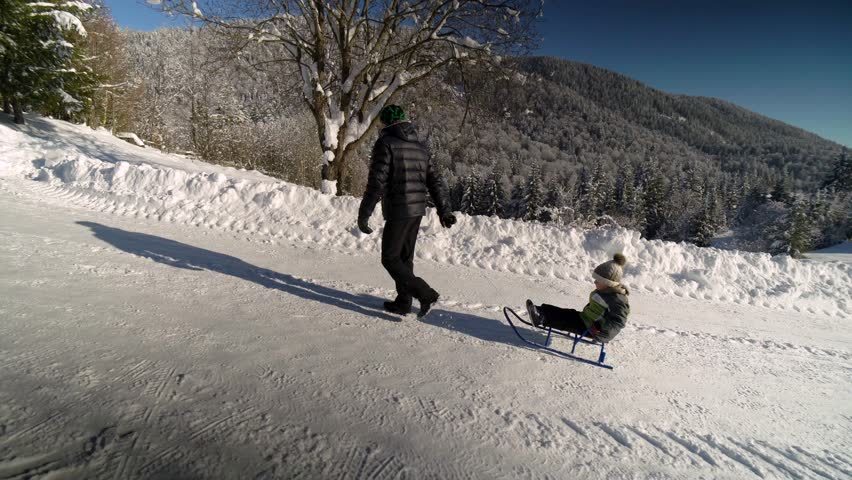Young happy family having fun playing in a snowy forest. Father rolls his little son on a sled. Dad and his little son are happy together. Winter sunny day.