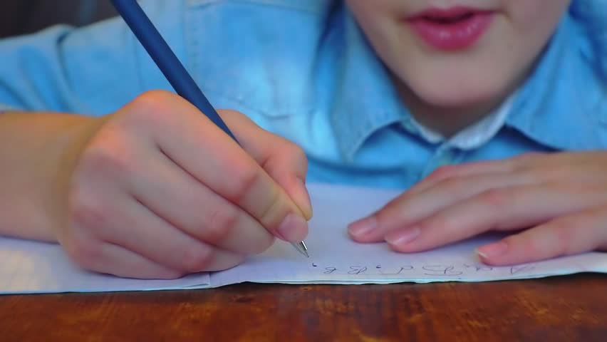 boy of school age writes in a notebook sitting at the table. Royalty-Free Stock Footage #1021622593