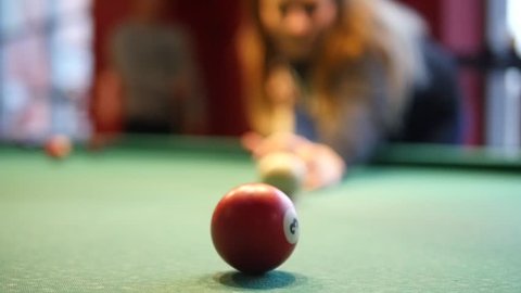 In a billiard club or a night club a women is playing billiard. In the background group of friends is visible. Concept: billiard game, pool, snooker, club, pub, entertainment, women's day 