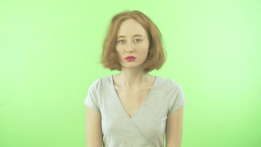 a young girl with a short red hair in a white T-shirt feels embarrassed. Isolated on a green background Royalty-Free Stock Footage #1021633855