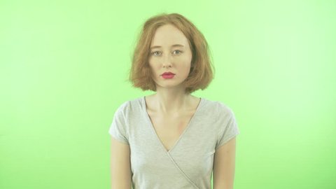 a young girl with a short red hair in a white T-shirt feels embarrassed. Isolated on a green background