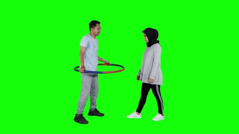 Happy young couple playing hula hoop in the studio. Shot in 4k resolution with green screen background