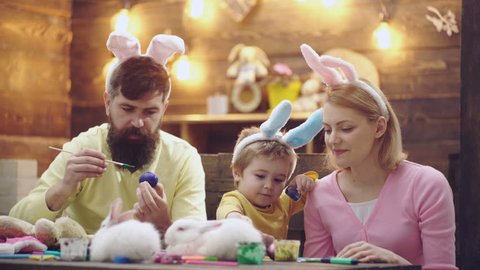 Little boy painting colorful eggs for easter with his parents. Family paints Easter eggs. Happy family are preparing for Easter. Cute little child boy wearing bunny ears