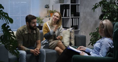Medium long shot of a reconciling young couple sitting in the office of a psychologist