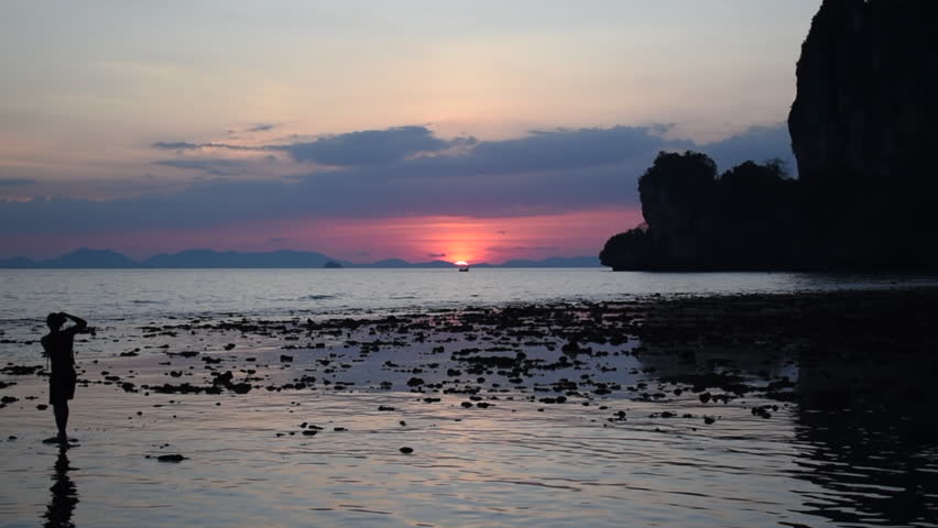 Silhouette of a photographer capturing a sunset on the ocean with a long boat passing in Railay Thailand