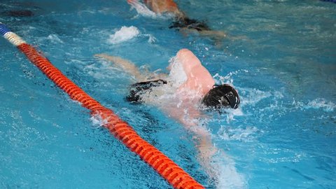 Close up for professional swimmer in slow motion while swimming race in indoor pool. Athlete training, swimming the crawl in the pool.