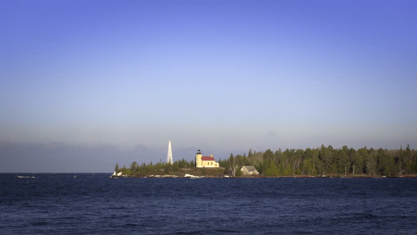 Lighthouse on Lake Superior with conifers around it. Gentle, fresh-water waves and lighthouse in foreground, winter, Upper Peninsula, Michigan. 4K UHD