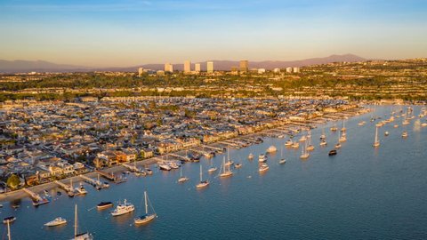 Aerial view and time lapse over Newport Beach harbor and coastal Orange County in California at sunset with boats and neighborhood beach homes below.